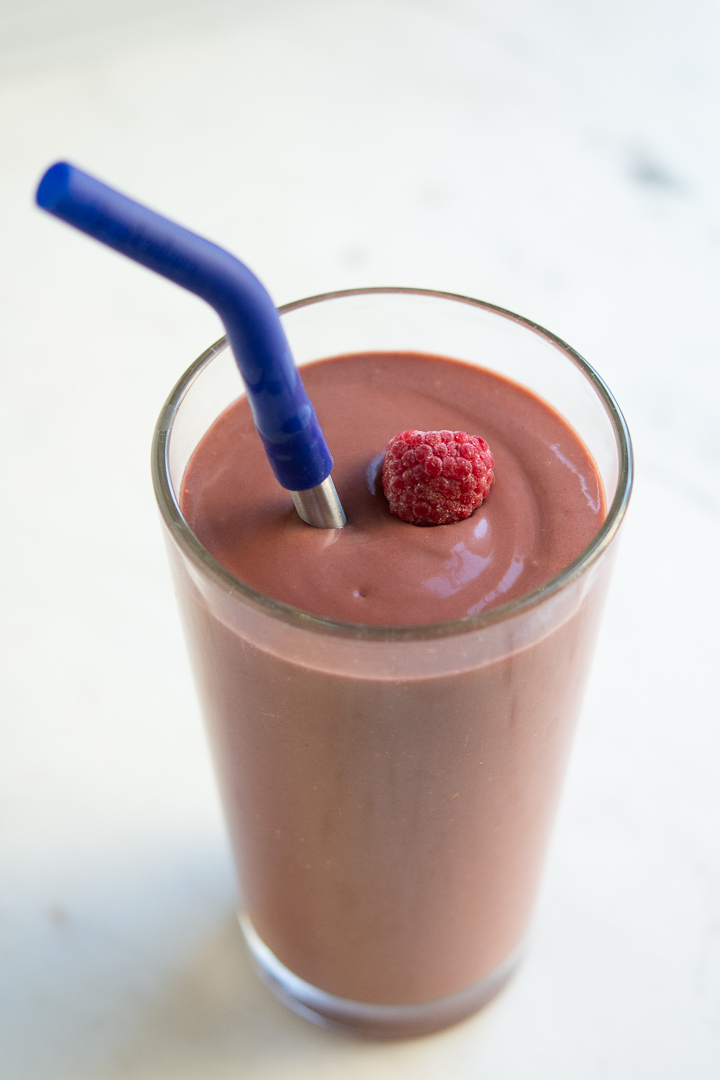 avocado raspberry and cocoa smoothie with straw and frozen raspberry on top