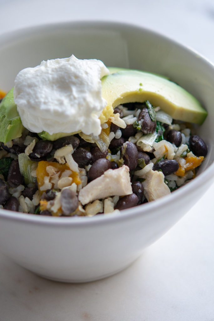 Photo of Chicken and Black Bean Skillet with Brown Rice in a bowl with greek yogurt and avocado