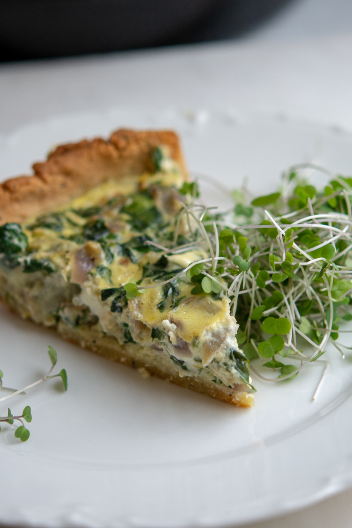 a piece of spinach and artichoke quiche on plate wth microgreens