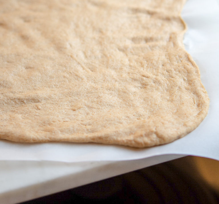 un-baked white whole wheat pizza dough on a baking sheet lined with parchment