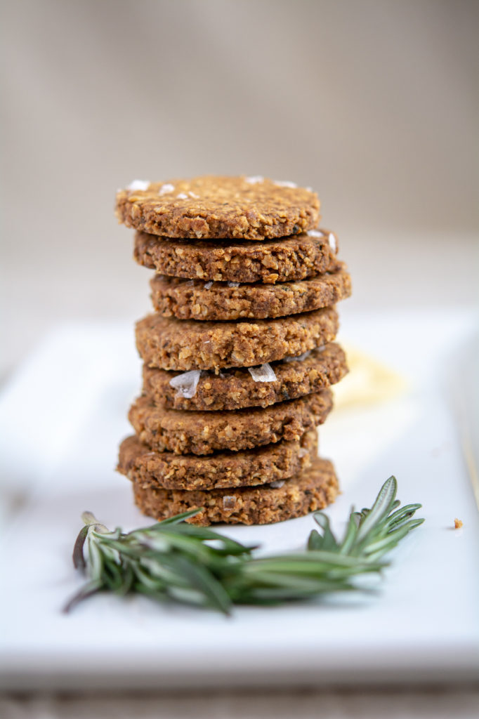 photo of rosemary oat crackers stacked on a white platter with rosemary