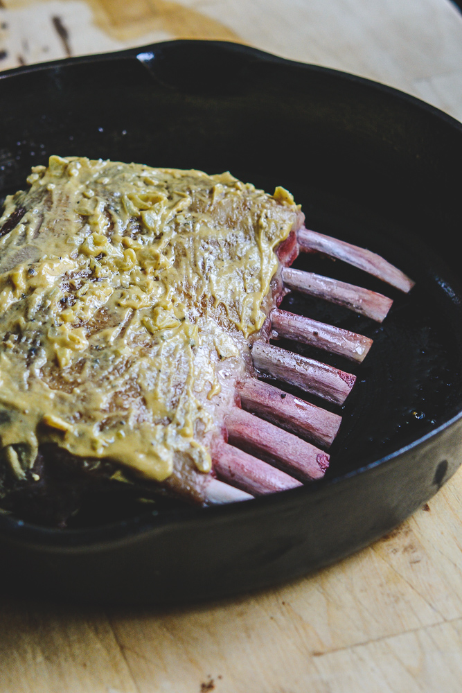 photo of rack of lamb in black cast iron skillet with mustard coating
