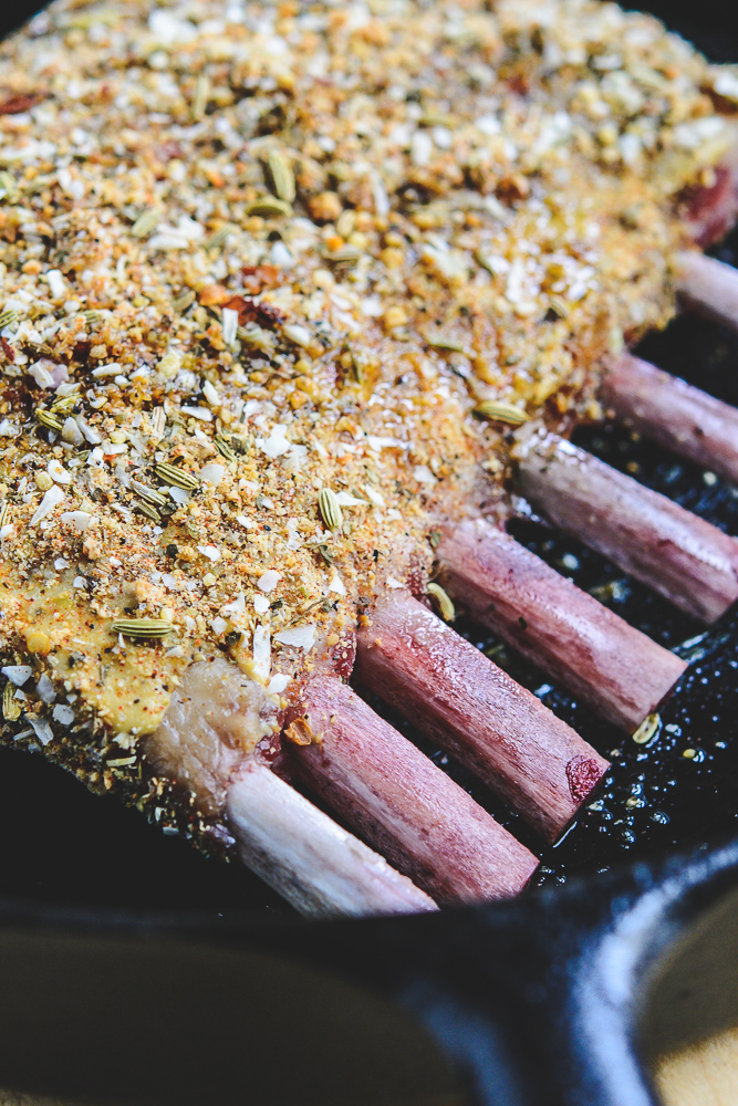 close up of photo of rack of lamb in black cast iron skillet with breadcrumb coating