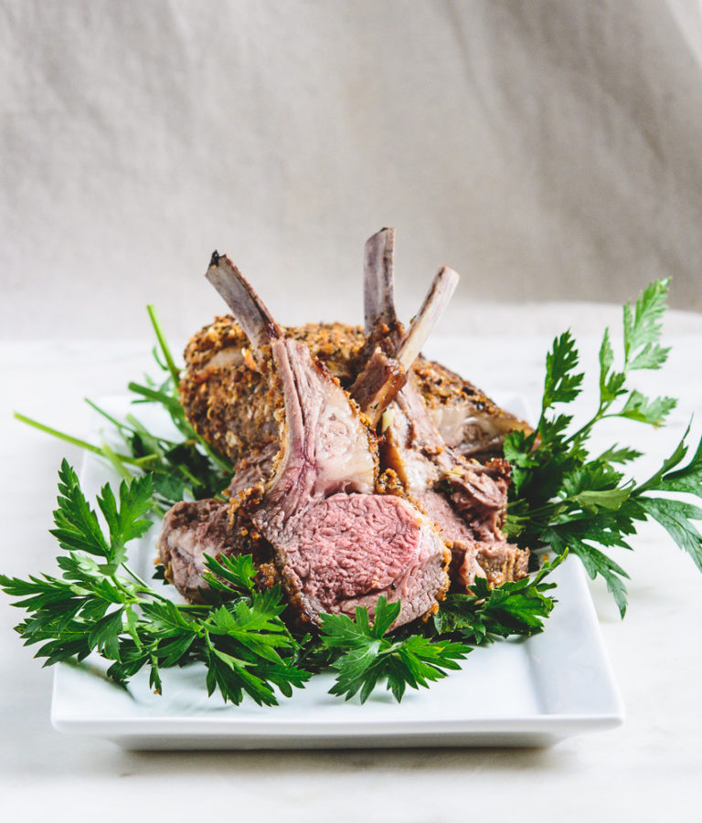 photo of rack of roasted lamb, cut in pieces on a bed of parsley on a white plate
