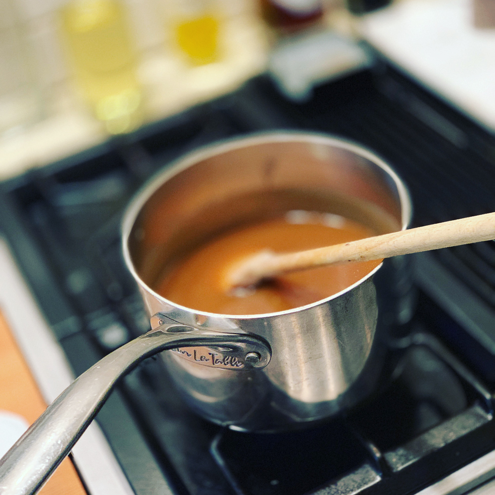 Caramel cooling on in a pan on the stovetop with a wooden spoon