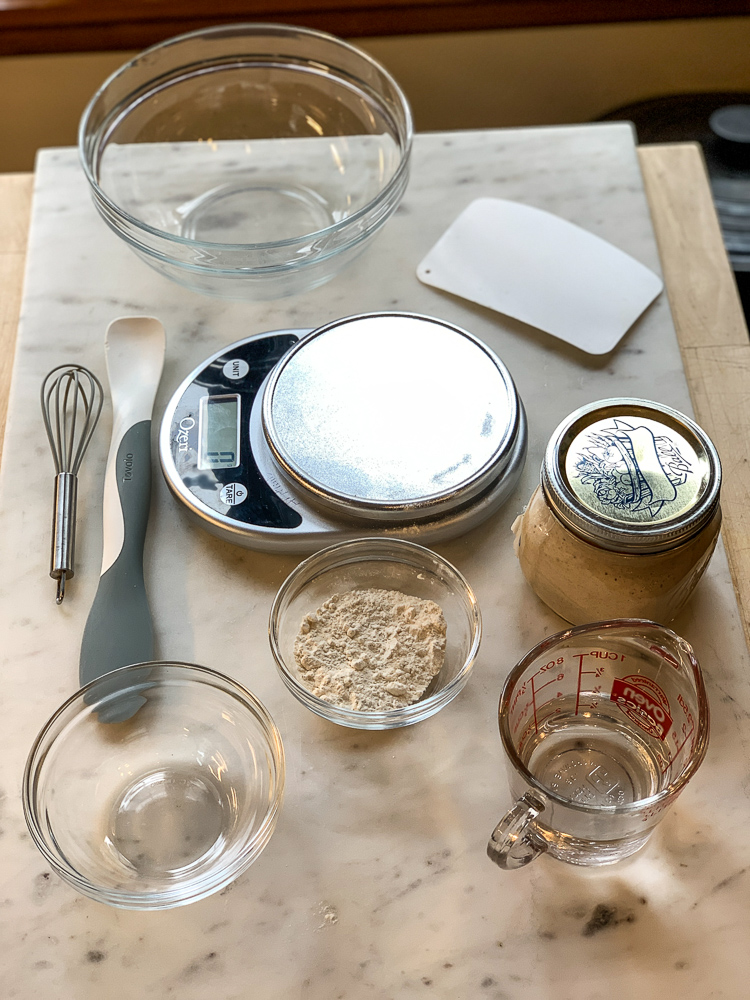 photo of various kitchen utensils for making sourdough bread. bowls, scale, dough scraper, whisk