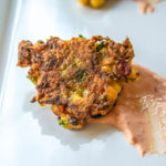 photo of single corn zucchini fritter with sauce on a white plate