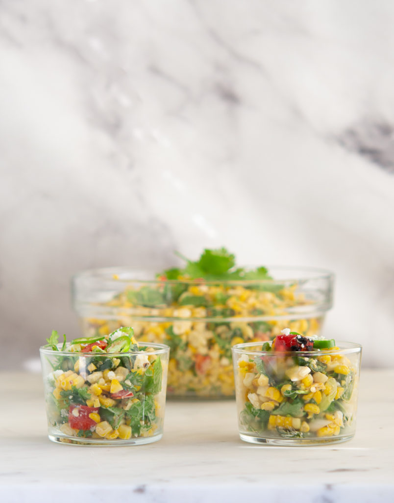 Straight on shot of two Grilled Elote Corn Salad in glass dishes with larger bowl behind