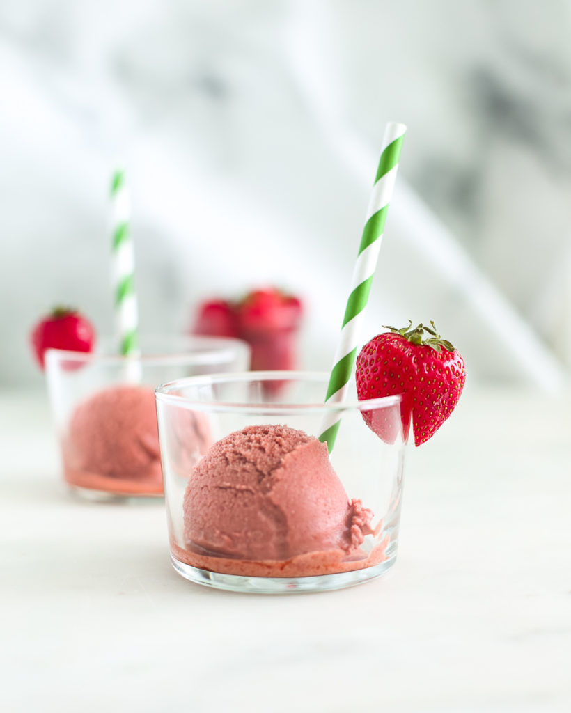 Strawberry Ice Cream in glass cup with a green paper straw