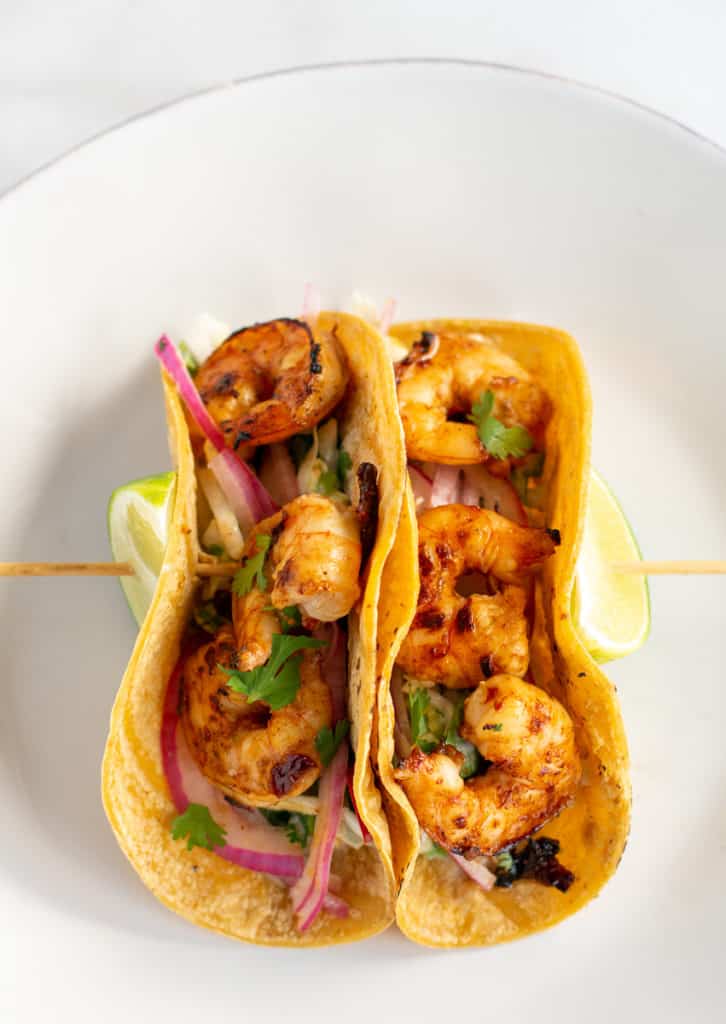 Overhead shot of Shrimp tacos on a skewer with lime wedges, vertical