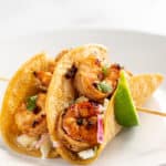 Shrimp tacos on a skewer with lime wedges, side view