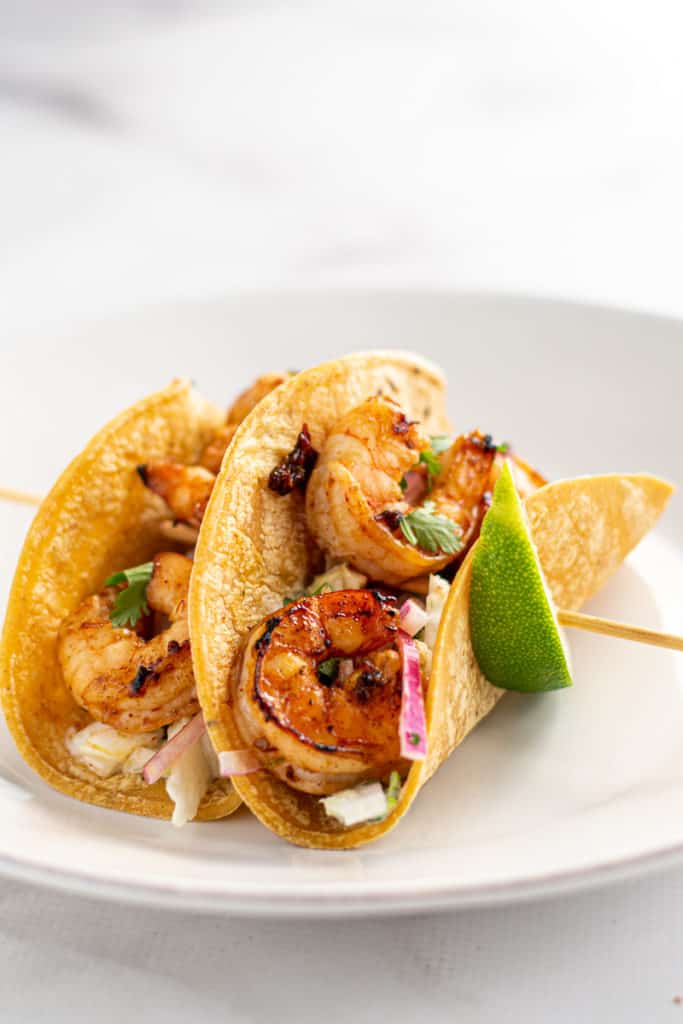 Shrimp tacos on a skewer with lime wedges, side view