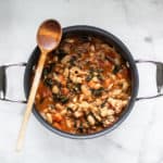 overhead shot of tuscan bean soup in black soup pot with wooden spoon