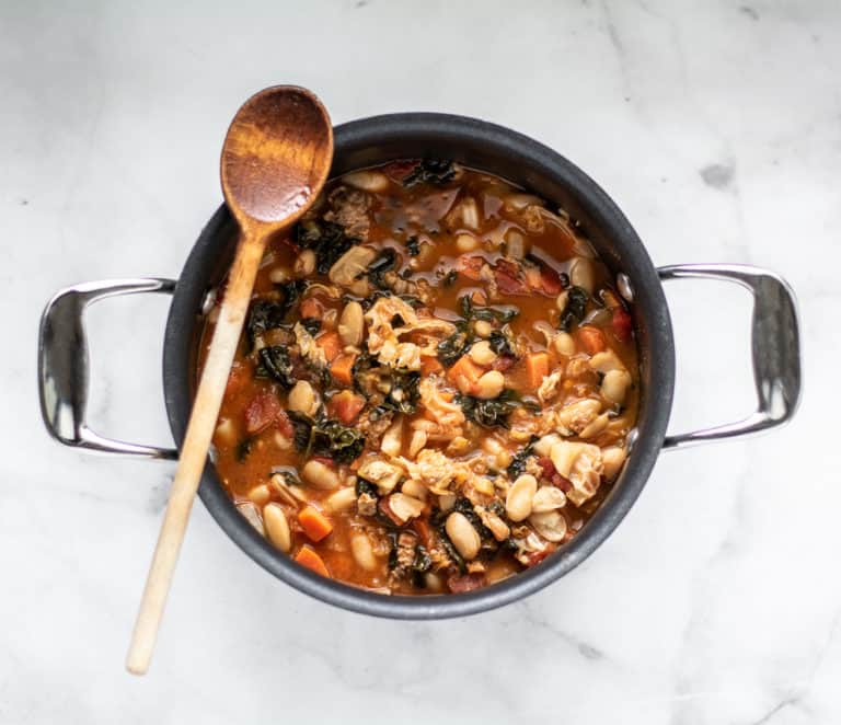 overhead shot of tuscan bean soup in black soup pot with wooden spoon