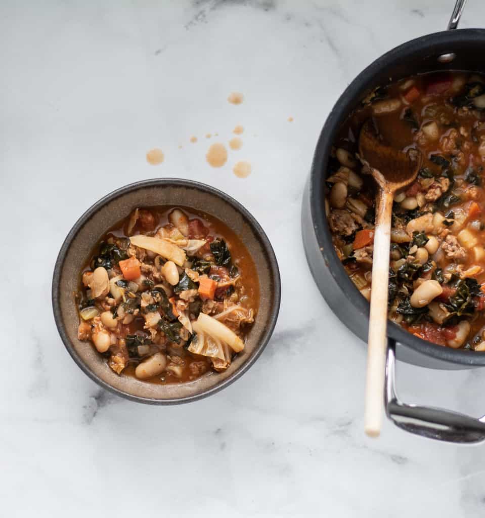 tuscan bean soup in brown bowl with pot of soup next to it