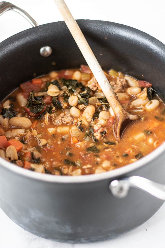 closeup of tuscan bean soup in black pot with wooden spoon