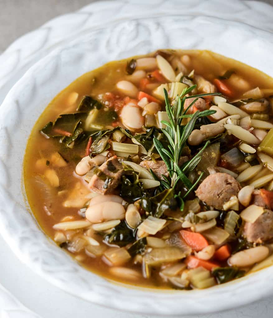 tuscan bean soup in a white bowl with rosemary garnish