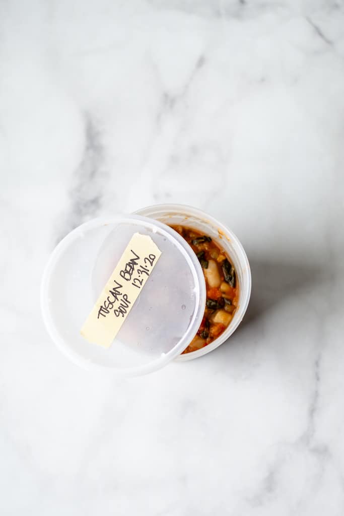 overhead shot of tuscan bean soup in takeaway container, with lid ajar