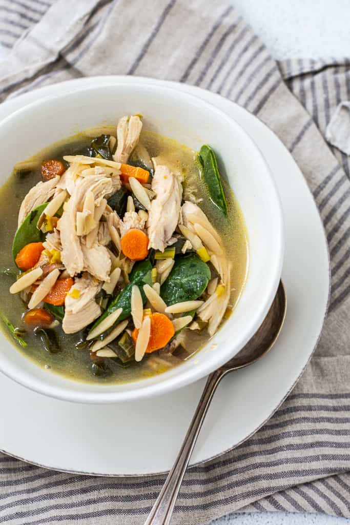 Over head shot of chicken soup with lemon and orzo with spoon and towel