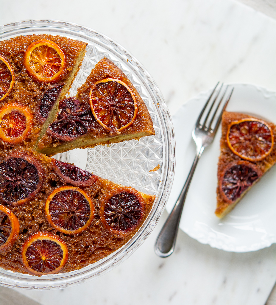 overhead shot of blood orange cake on a cake plate and a piece on a white plate