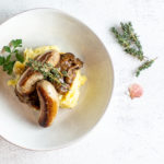 bangers and mash in a shallow bowl with thyme and lucky shell as garnish