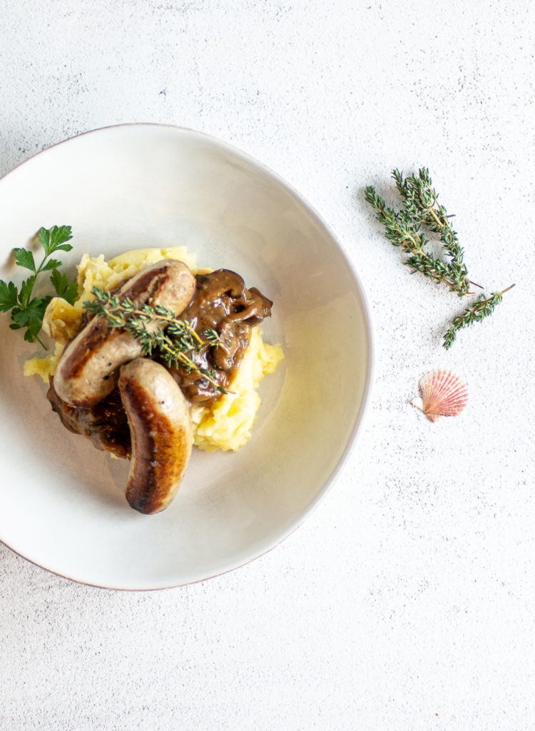 bangers and mash in a shallow bowl with thyme and lucky shell as garnish