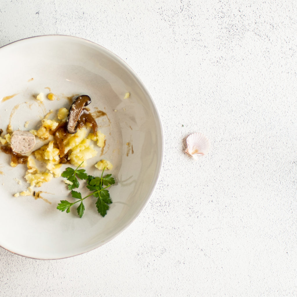 Empty bowl of bangers and mash with shelagh's lucky shell beside the bowl