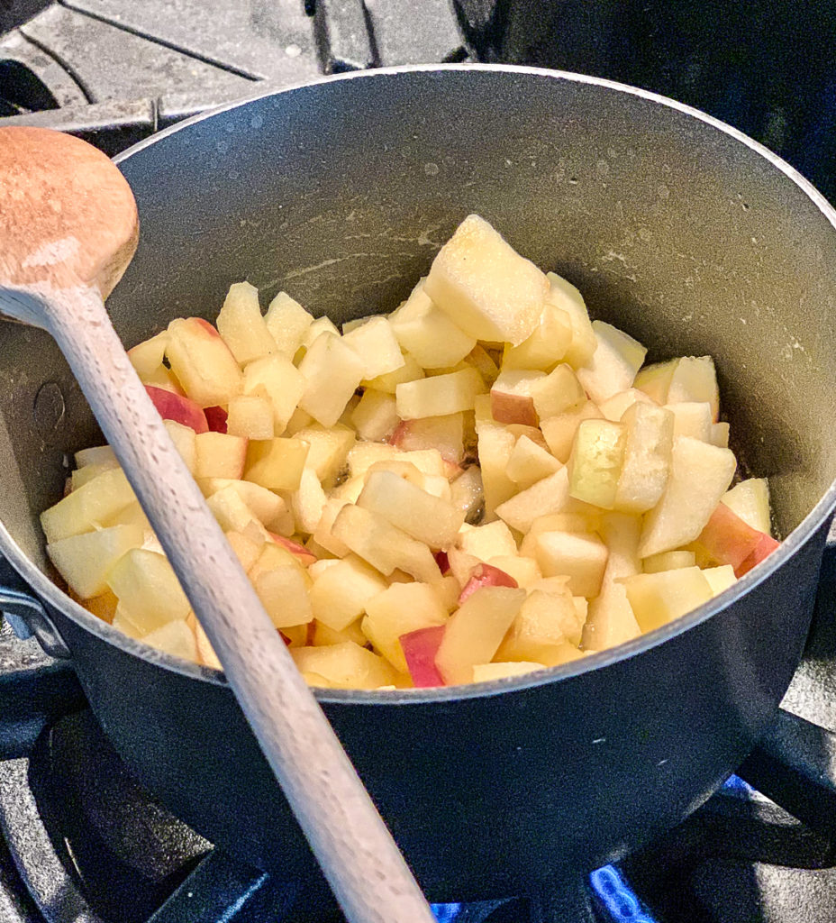 apples sauteeing in a pan on gas stove, with wooden spoon