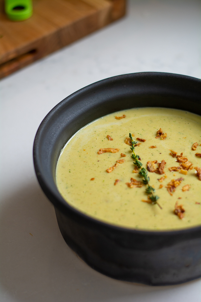 leek and potato soup in a ceramic pot with crispy onions and a sprig of thyme