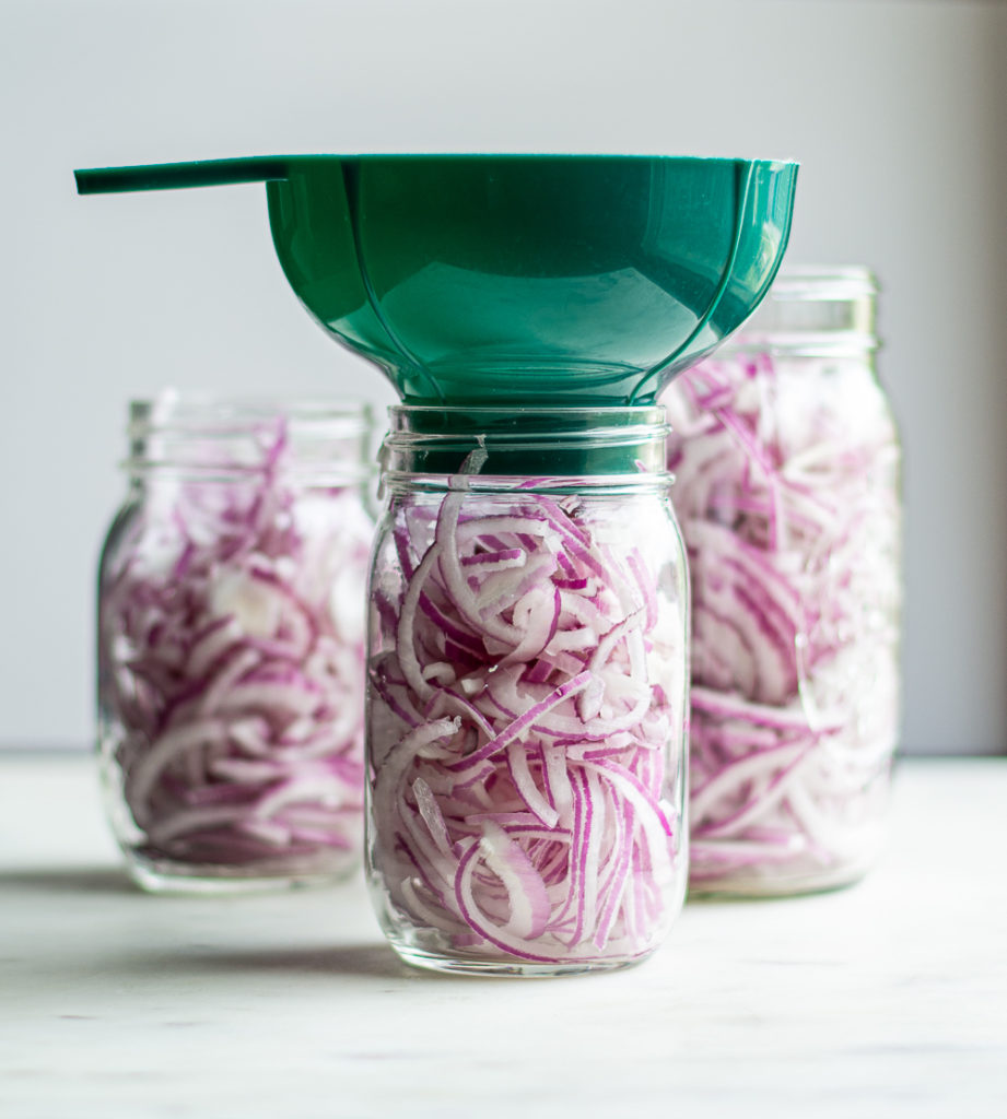 red onions in mason jars with a green funnel