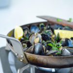 garlicky guinness mussels in a pan with lemon wedges