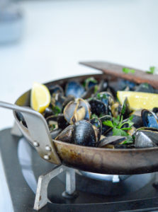 garlicky guinness mussels in a pan with lemon wedges