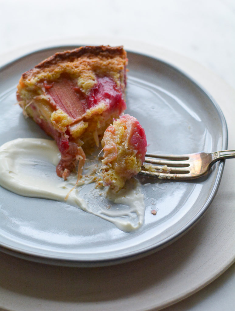 rhubarb cake on a plate with a schmear of sauce being cut with a fork