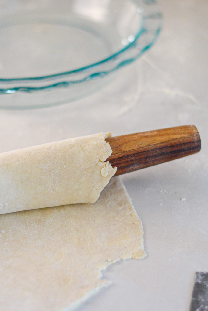 pie dough on a rolling pin with glass pie plate