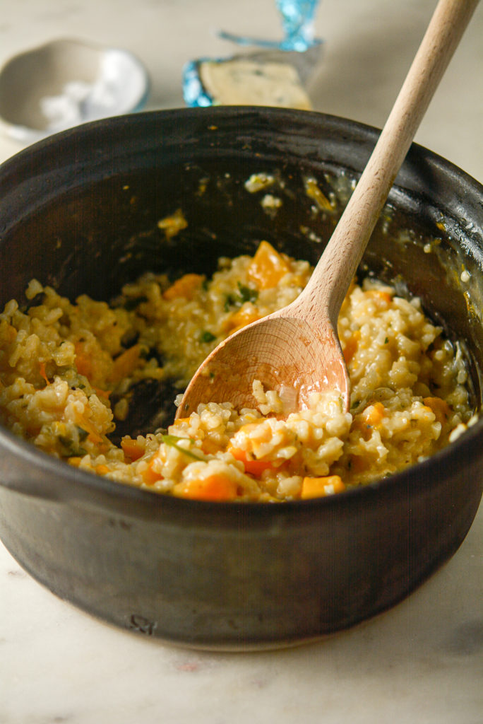 Winter squash risotto with Gorgonzola in a clay cooking pot with a wooden spoon