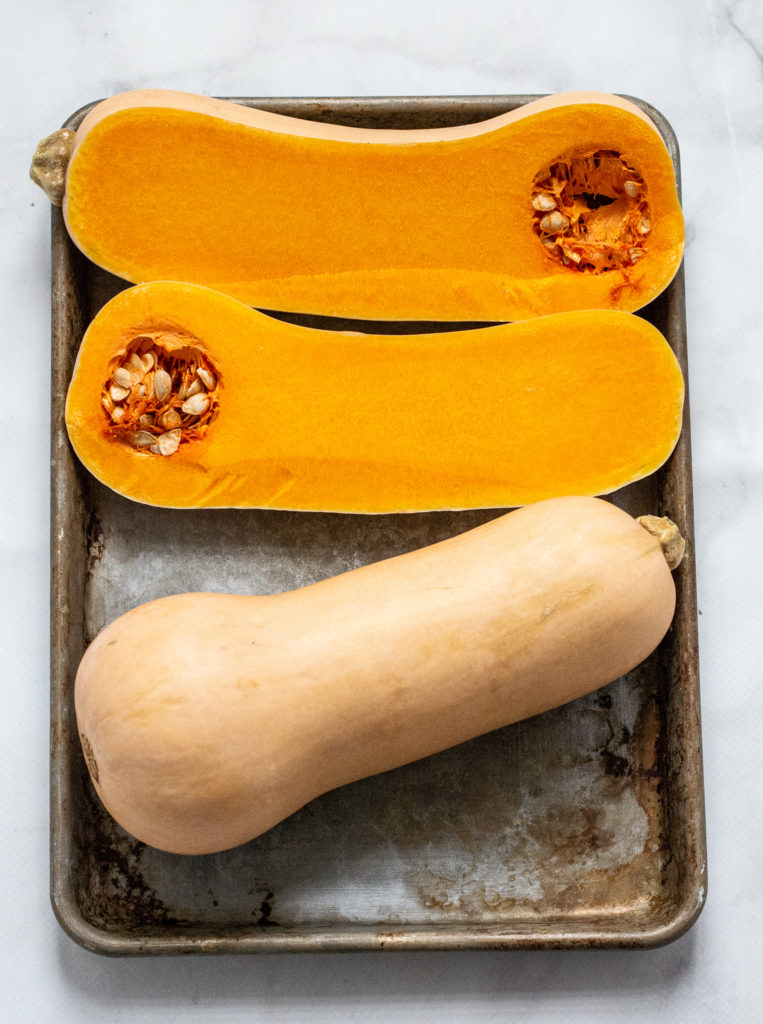 butternut squash on a rimmed baking sheet, one whole, one cut down the center