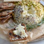 cheeseball portion spread on a cracker, on a round cutting board