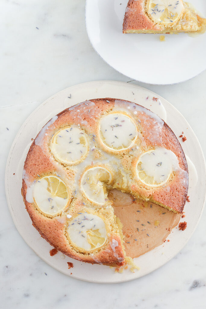 Photo of lemon olive oil cake with lemon drizzle iwth a piece out of it and lavendar garnish