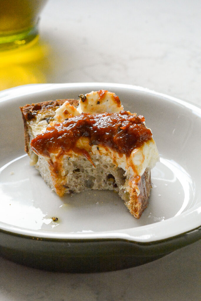Black Garlic and Tomato Chutney on a spoon with bread and goat cheese and a bite out of the bread
