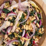 Overhead shot of Kale Peanut Salad with Chicken in a wooden bowl with dressing