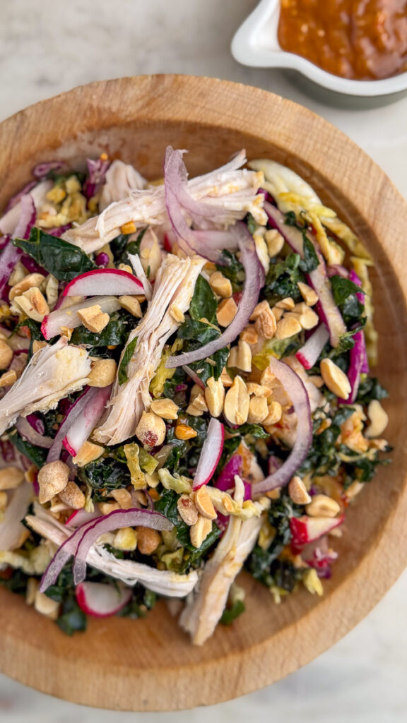 Overhead shot of Kale Peanut Salad with Chicken in a wooden bowl with dressing