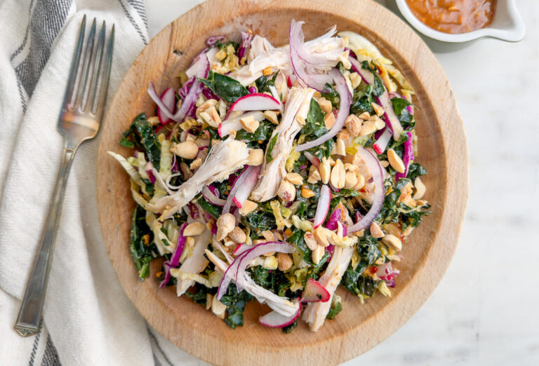 Overhead shot of Kale Peanut Salad with Chicken in a wooden bowl and fork